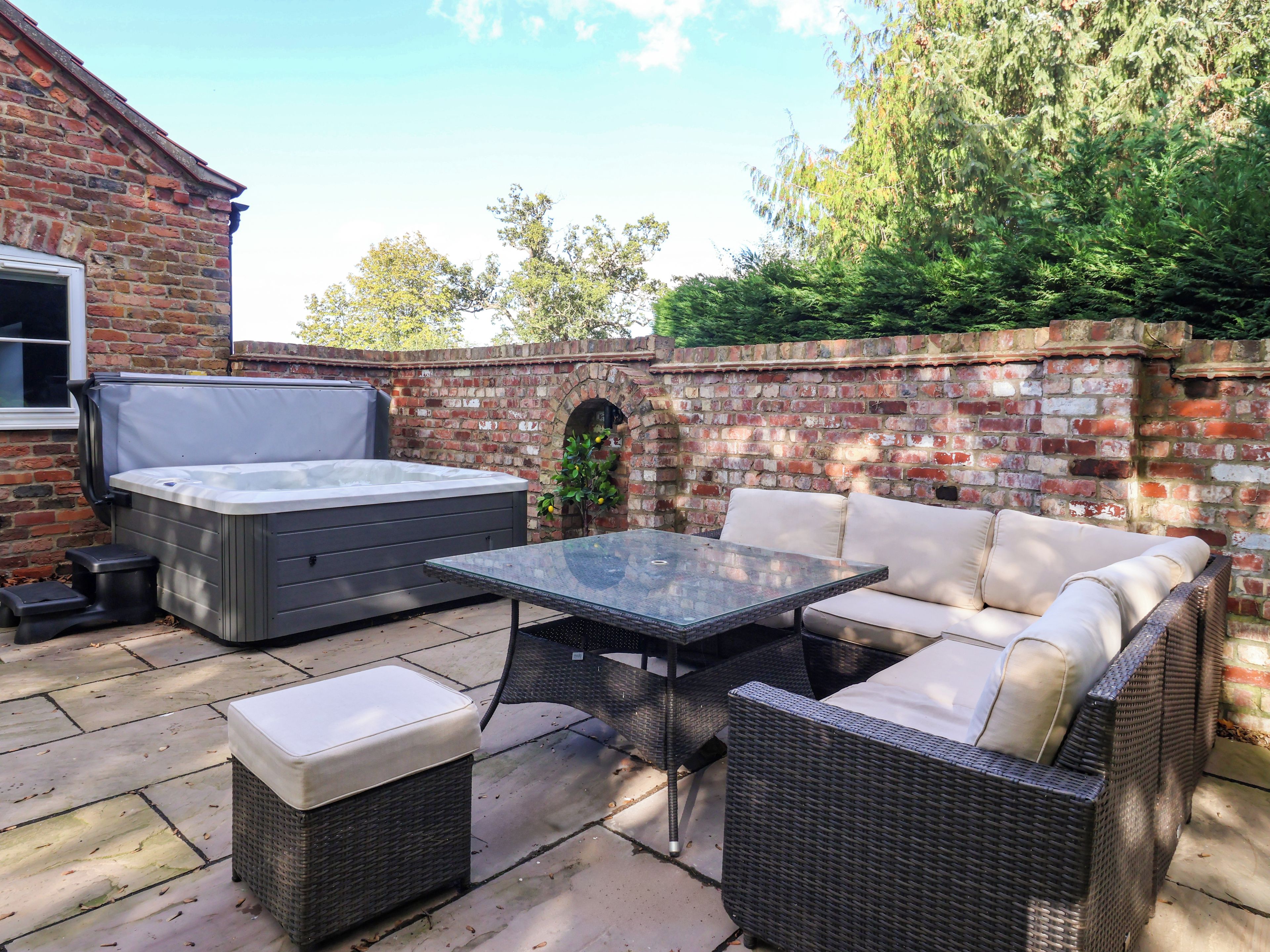 An outdoor patio with a hot tub, a glass-top table, wicker furniture, and a brick wall.