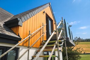 Ein Haus mit Holzwand und schwarzem Dach, umgeben von blauem Himmel.