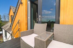 Ein Balkon mit Korbmöbeln und einem Glastisch, mit Blick auf eine reizvolle Landschaft.