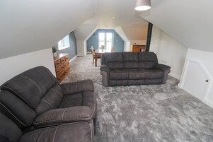 Habitación en ático con alfombra gris, dos sofás oscuros, un aparador de madera y una mesa de comedor con sillas.