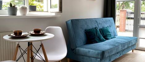 A room with a blue sofa, a white chair, a small round table with two cups, and a hanging light fixture.
