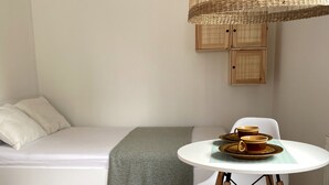 A small, cozy room with a white sofa, a round table with a tray of cups, a woven hanging light fixture, and a pair of wooden cabinets. - Apartment for 2 People Near the sea (Mielno)