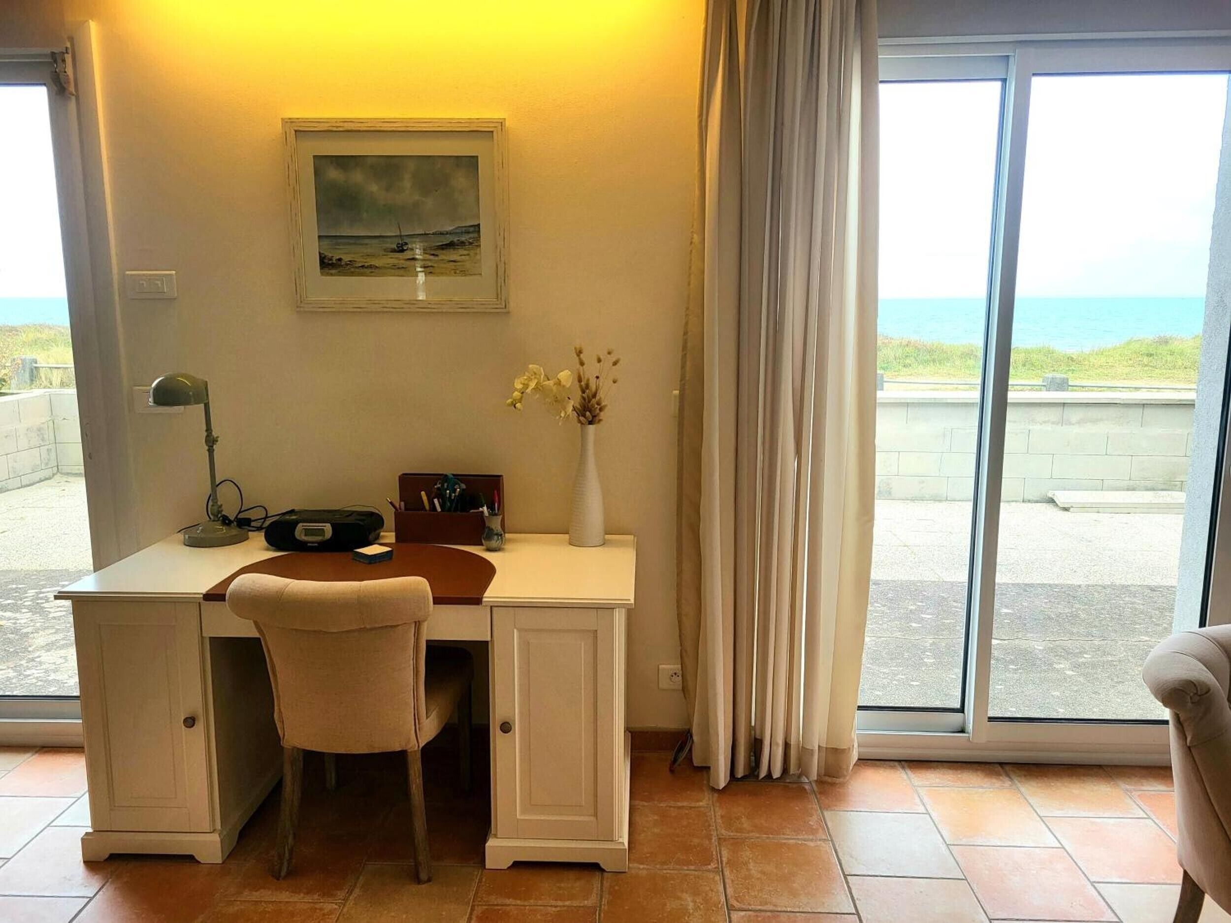Ein Zimmer mit Schreibtisch, Stuhl und Blick auf das Meer durch ein großes Fenster.