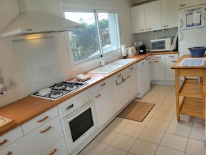 Una cocina moderna con armarios blancos, encimera de madera, estufa a gas, horno, microondas y fregadero.