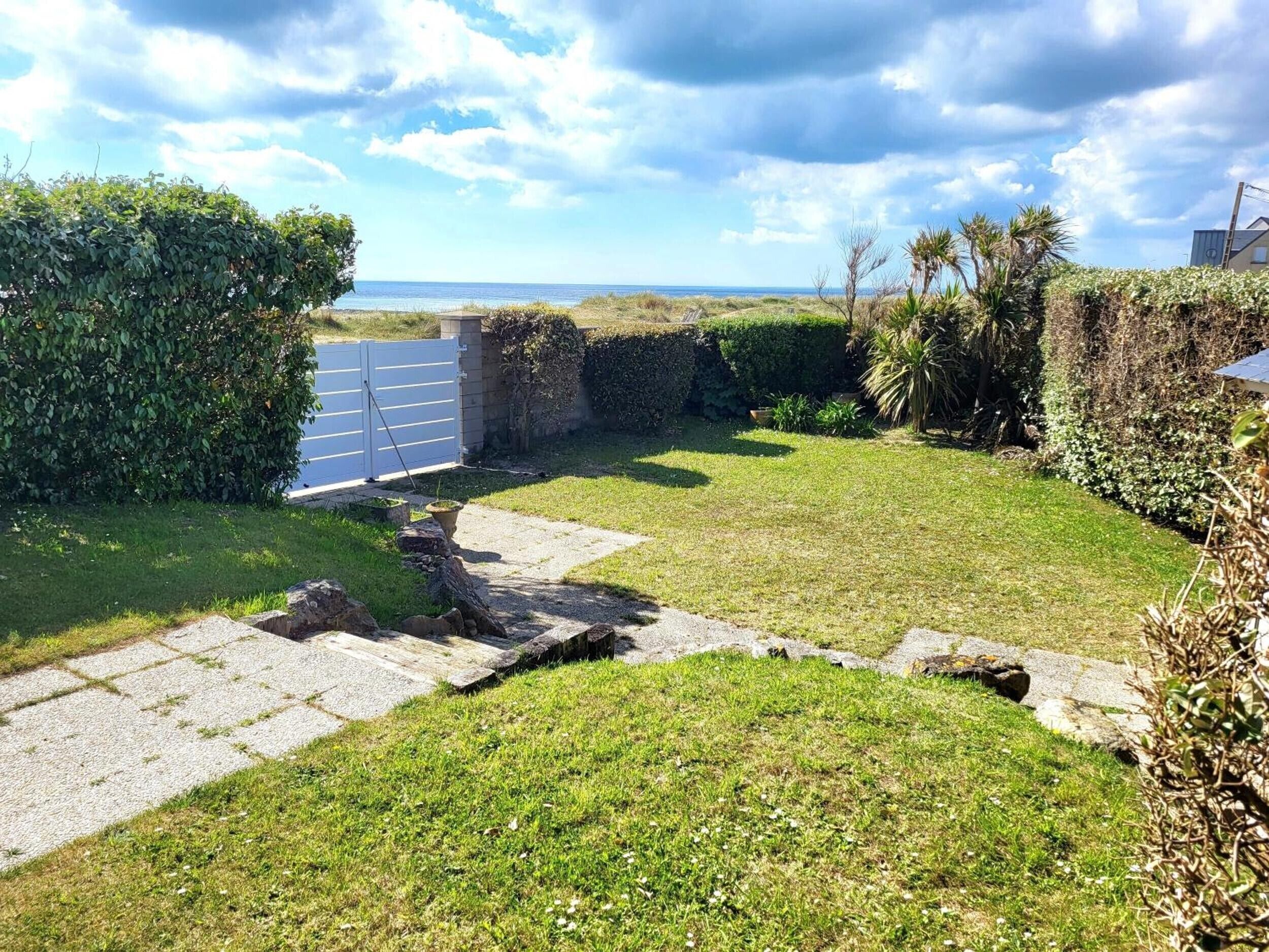 Un jardin bien entretenu, avec un chemin dallé menant à une entrée fermée par un portail.