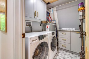 A compact laundry room with a front-loading washer and dryer, a towel rack, and a water heater.