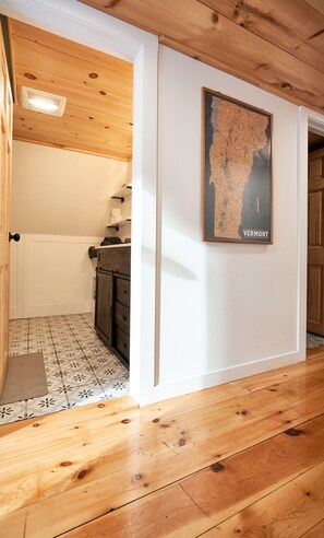 A wooden interior with a map of Vermont on the wall, a kitchen area with cabinets, and a patterned floor.