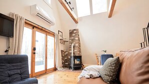 A living room with a sofa, a television, a fireplace, and a large window. - Cozy, Private Dog-Friendly A-Frame Cabin: Mins to Hiking + Adorable Towns (Weathersfield)