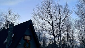 A cabin with a sloped roof, a visible chimney, and a lit interior. - Cozy, Private Dog-Friendly A-Frame Cabin: Mins to Hiking + Adorable Towns (Weathersfield)