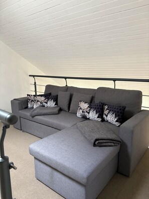 A grey sectional sofa with patterned cushions, a matching ottoman, and a metal railing. - House in the heart of nature (Gabriac)