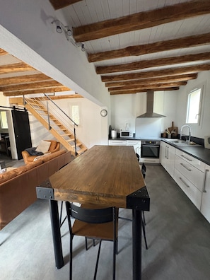 A modern kitchen with a wooden table, black chairs, and a staircase leading to a living area with a sofa. - House in the heart of nature (Gabriac)