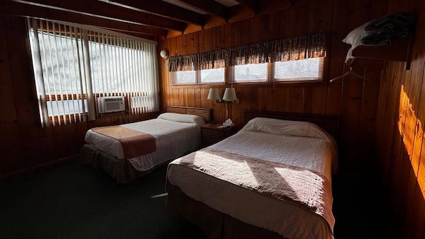 A room with two beds, a window with blinds, a lamp, and a wall-mounted heater. - Cozy 1BR hotel room, Hamilton - #349 Iroquois (Hamilton)