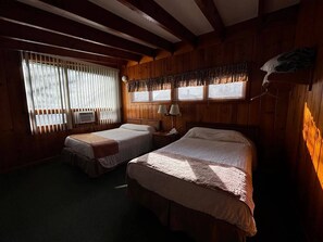 Ein Zimmer mit zwei Betten, einem Fenster mit Jalousien, einer Lampe und einem Wandheizgerät.