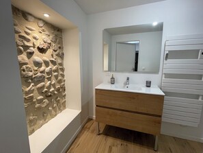 Une salle de bain avec un mur en pierre, un lavabo blanc et un miroir.