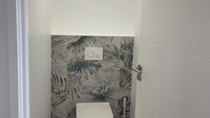 Ett litet, smalt badrum med en toalett, en radio som är monterad på väggen och en taklampa.