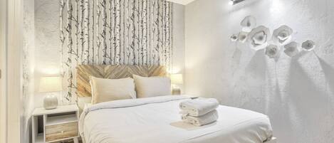 Habitación de hotel con cama, mesitas de noche, una pared con un estampado de árbol y una pared con diseño floral.