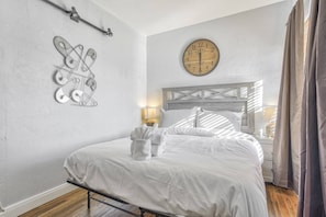 A bedroom with a wooden headboard, a wall clock, and a metal wall art piece.