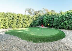 A well-maintained golf course with a putting green, two flags, and a dense hedge in the background. - Stylish 2-Bedroom Indio Retreat with Pool, A/C, and Modern Comforts (Indio)