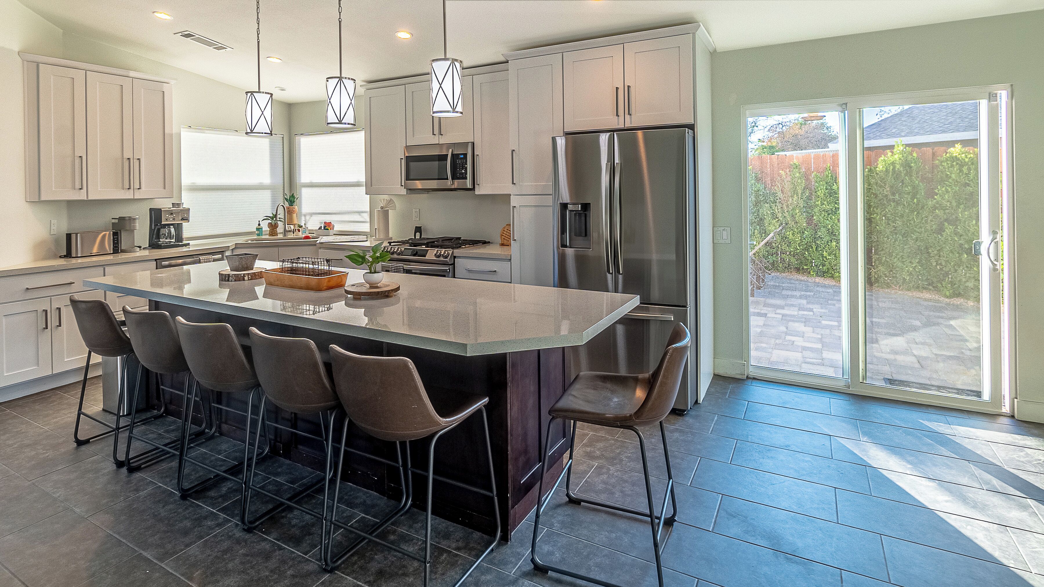 A modern kitchen with a large island, bar stools, stainless steel appliances, and a view to the outside.
