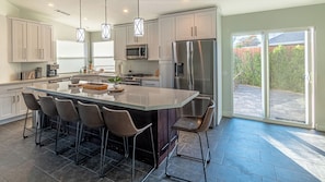 A modern kitchen with a large island, bar stools, stainless steel appliances, and a view to the outside. - Stylish 2-Bedroom Indio Retreat with Pool, A/C, and Modern Comforts (Indio)