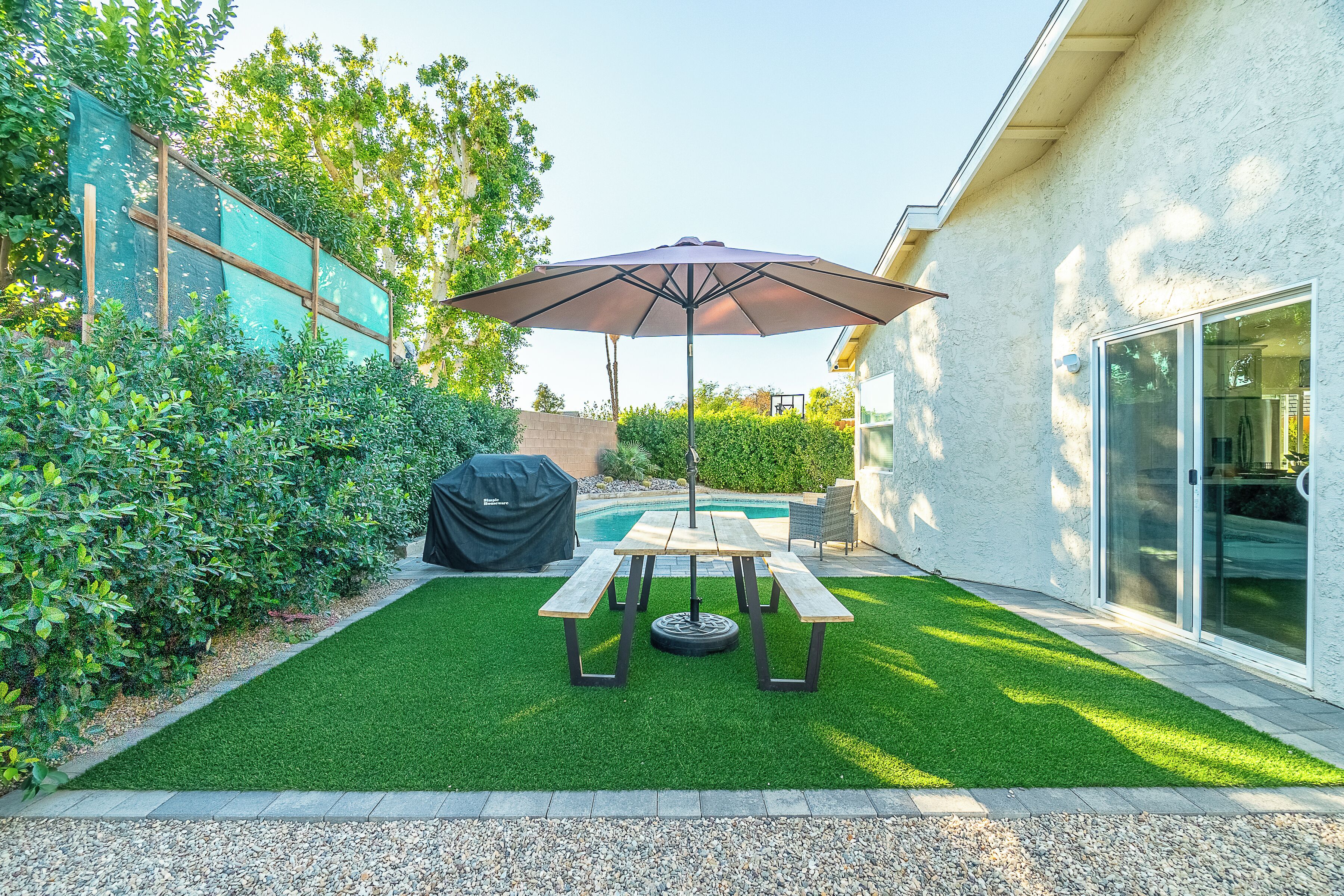 A patio with a table and umbrella, surrounded by a well-maintained lawn and a pool.