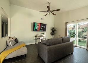 A living room with a grey sofa, a small table, a TV, and a ceiling fan. - Stylish 2-Bedroom Indio Retreat with Pool, A/C, and Modern Comforts (Indio)