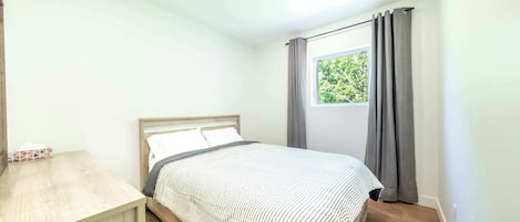 Makuuhuoneessa on yksi sänky, ikkunassa on verhot ja huoneessa on puinen yöpöytä.