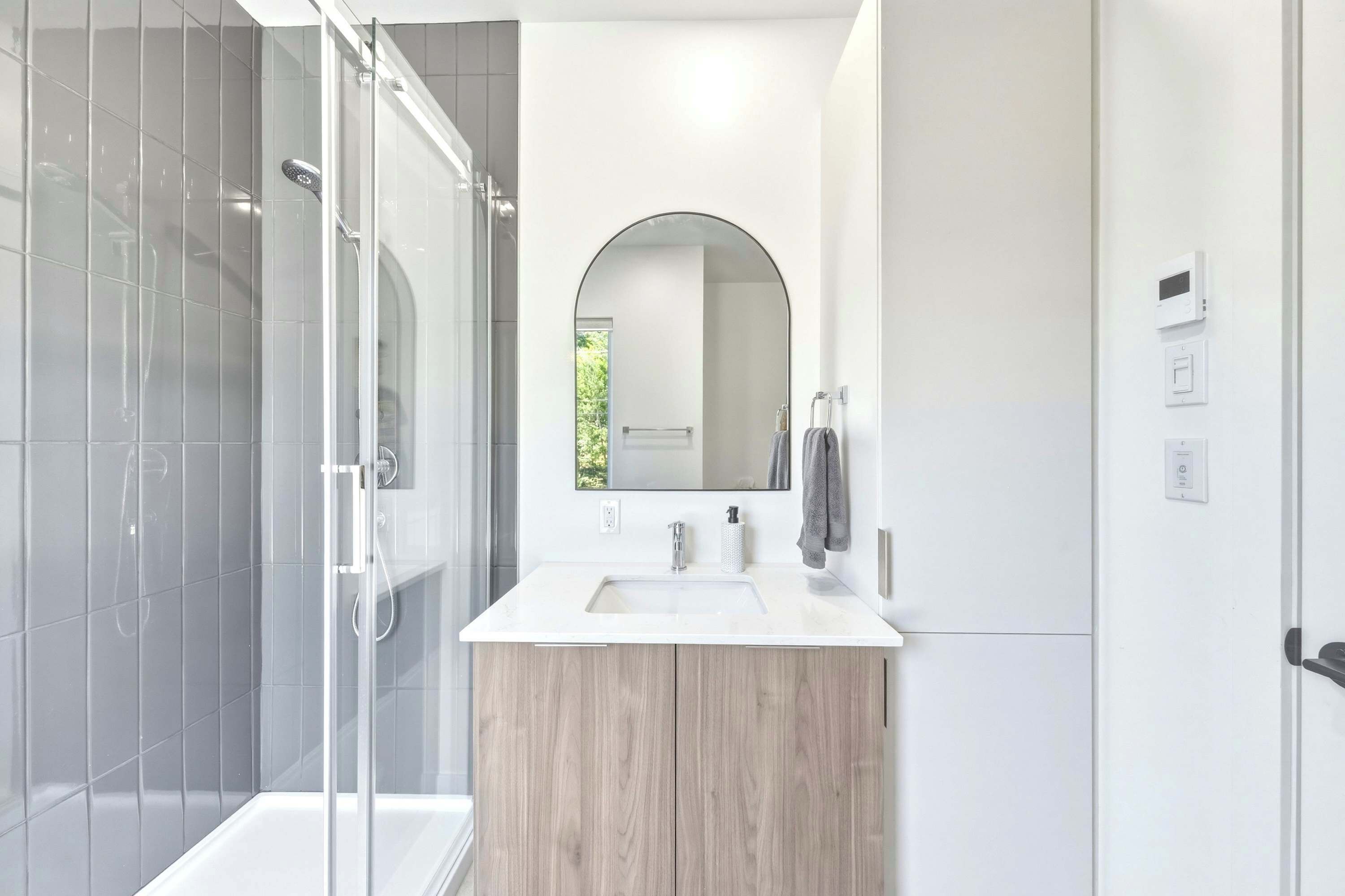 Une salle de bain moderne avec une douche à parois de verre, un meuble-lavabo en bois, un grand miroir et un lavabo blanc.