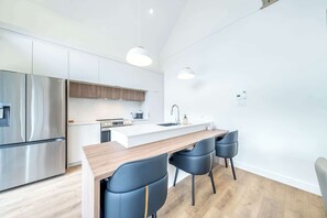 A modern kitchen with stainless steel appliances, a wooden countertop, and black chairs.