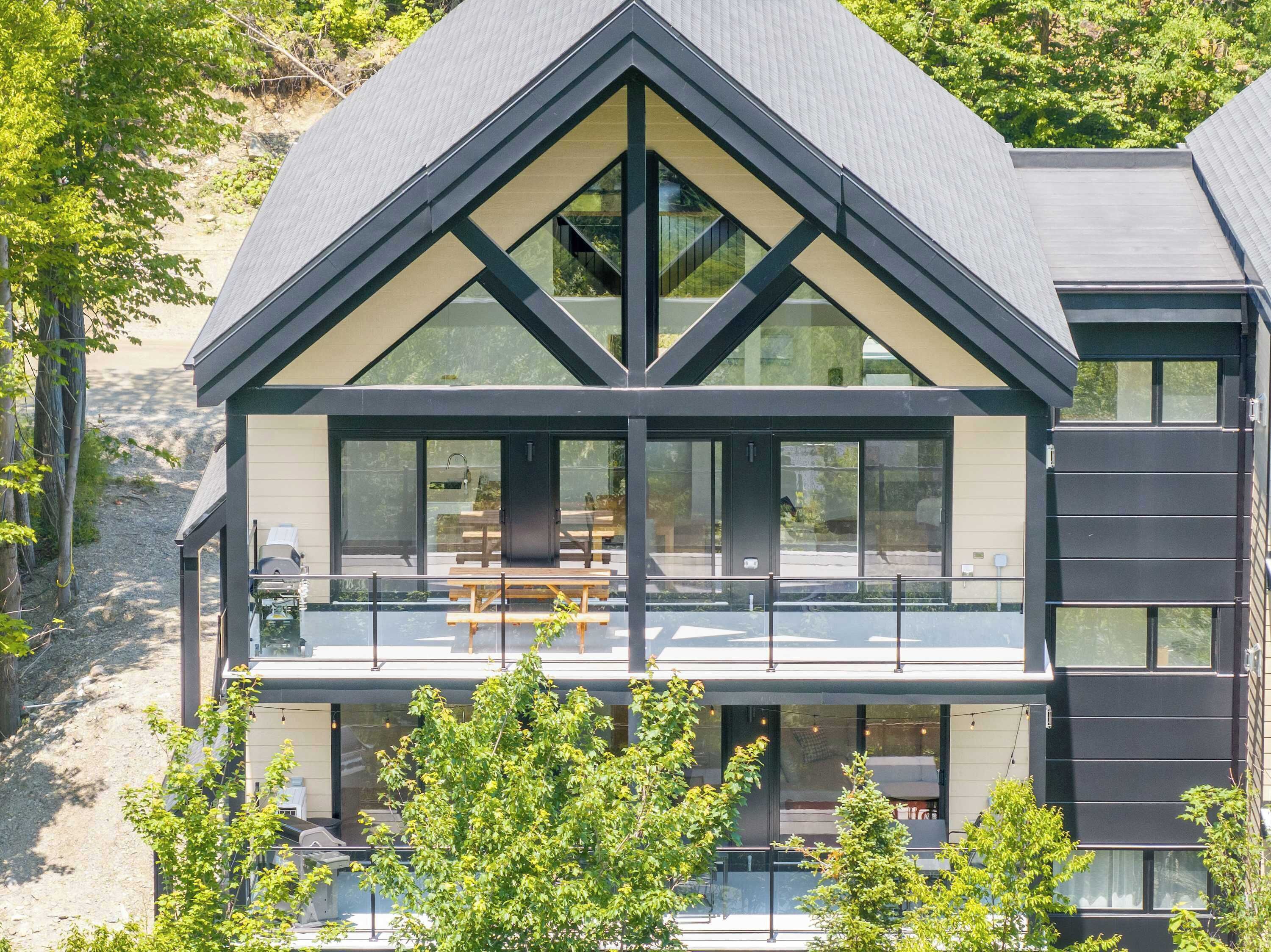 A modern two-story house with a balcony, large windows, and a sloped roof.
