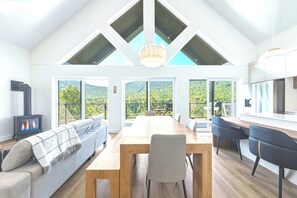 A spacious room with a high ceiling, a wooden dining table, a sofa, and a kitchen area with a stove.