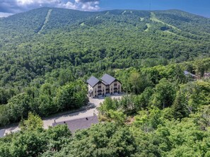 A two-story building with a symmetrical roof and a central entrance, surrounded by dense forest and hills.