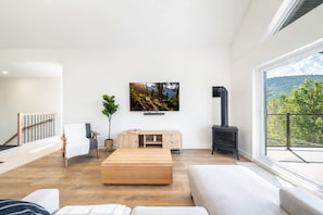 A modern living room with a large window, a fireplace, a flat-screen TV, and a wooden bench.