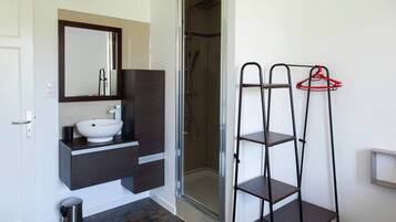 Een badkamer met een witte wasbak, donkere kastjes, een spiegel en een douchecabine.