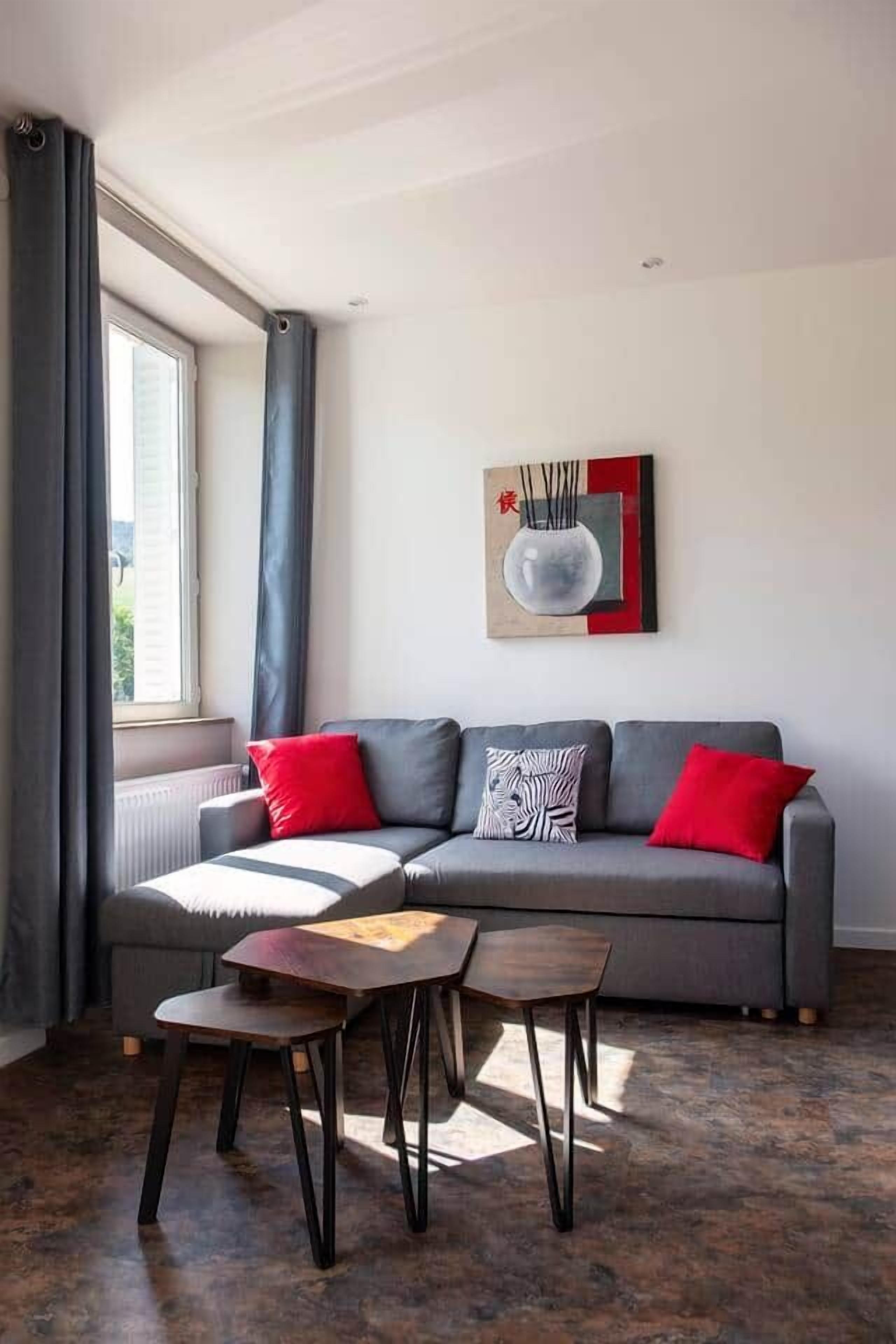 A modern living room with a grey sofa, red cushions, a small wooden table, and a floor lamp.