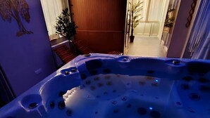 A hot tub with multiple jets, a wooden floor, and a view of a hallway with a plant.