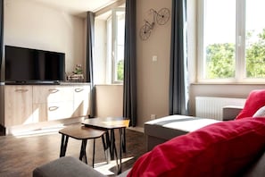 A modern living room with a television, a small table, a sofa, and a window with curtains.