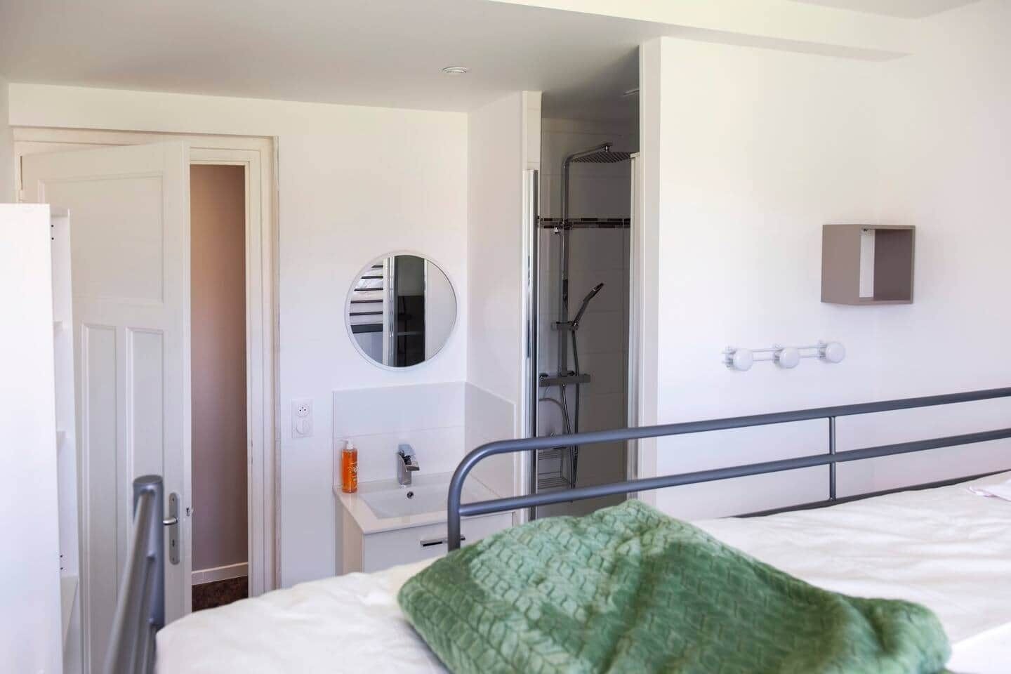 A hotel room with a bed, a bedside table, a mirror, a shower area, and a small cabinet.