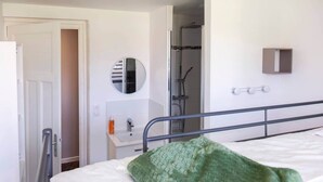 A hotel room with a bed, a bedside table, a mirror, a shower area, and a small cabinet.