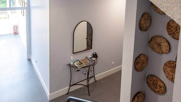 A hallway with a small table holding magazines and a bottle, a mirror on the wall, and a textured wall with circular patterns.