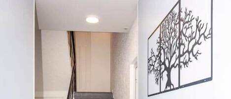 A staircase with a handrail, a radiator on the wall, and a framed artwork depicting a tree.