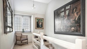 A hallway with a white staircase, a painting, a bust, and a chair. - Raphael Rooms (Peterborough)