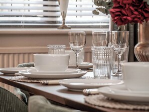 A dining table set with plates, bowls, and glasses, with a window and blinds in the background. - Raphael Rooms (Peterborough)