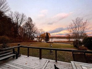 Eine Holzterrasse mit Geländer, die auf einen See mit umliegenden Bäumen und Rasenflächen blickt.