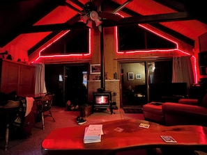Ein gemütliches Zimmer mit Kamin, Holzbalkendecke und roter Neonleuchte als Akzent.