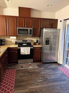 A kitchen with wooden cabinets, a stainless steel refrigerator, a microwave, and a stove. - Spacious 4-bedroom townhome Cary/Morrisville area (Cary)