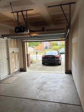 A garage with a car parked outside, a metal structure overhead, and a concrete floor. - Spacious 4-bedroom townhome Cary/Morrisville area (Cary)
