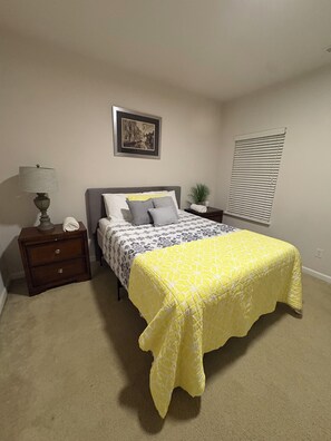 Una camera da letto con un letto, un comodino, una lampada, un quadro e una finestra.