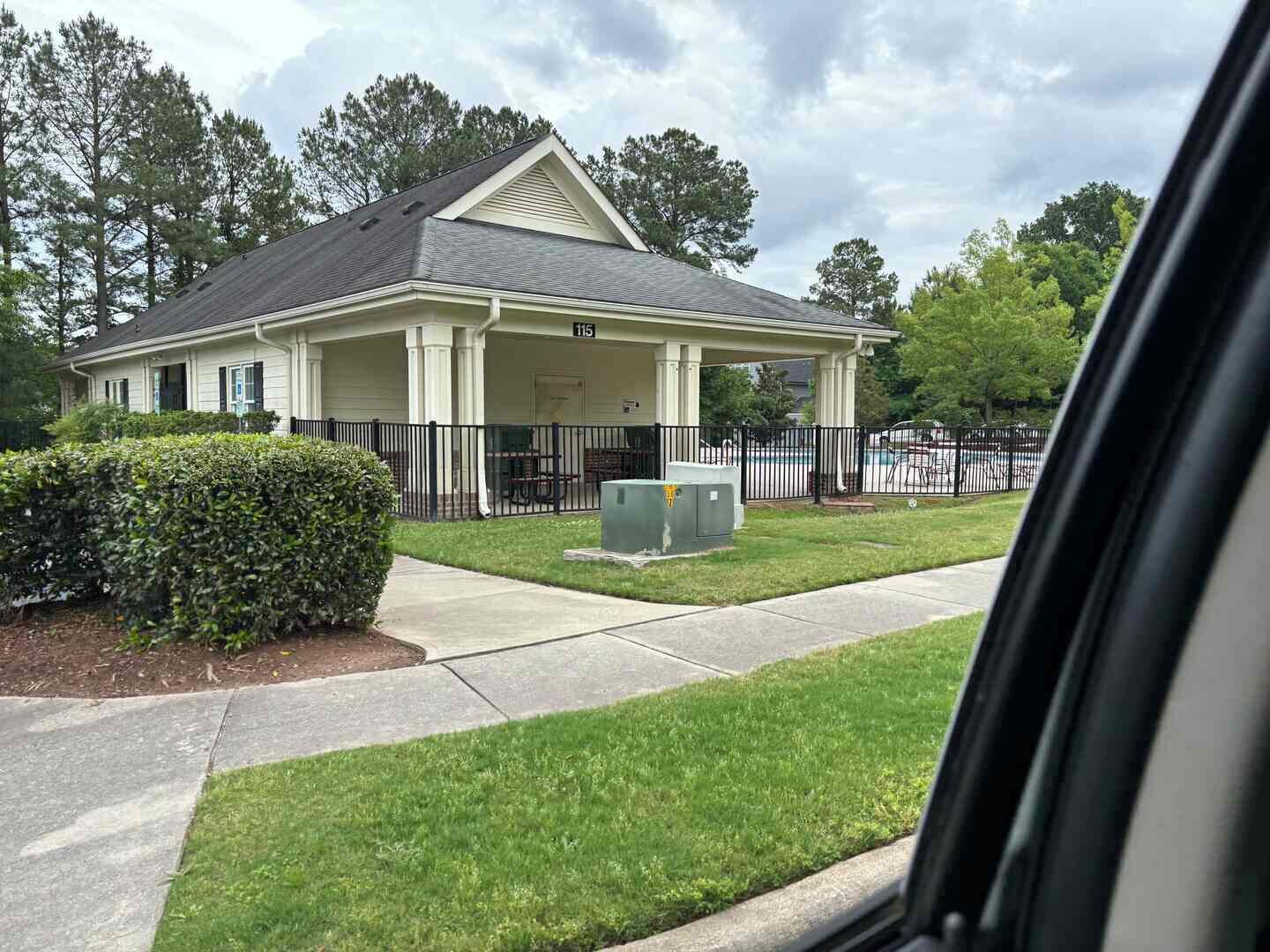A two-story house with a covered porch, a fenced yard, and a swimming pool in the background.