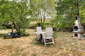 An outdoor seating area with a table and chairs, a stone-built fireplace, and a statue.